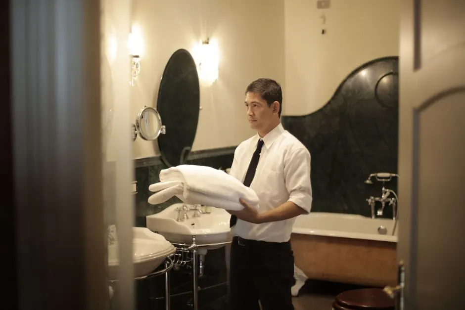 Side view of young male employee holding stack of white towels while standing in bathroom of luxury hotel
